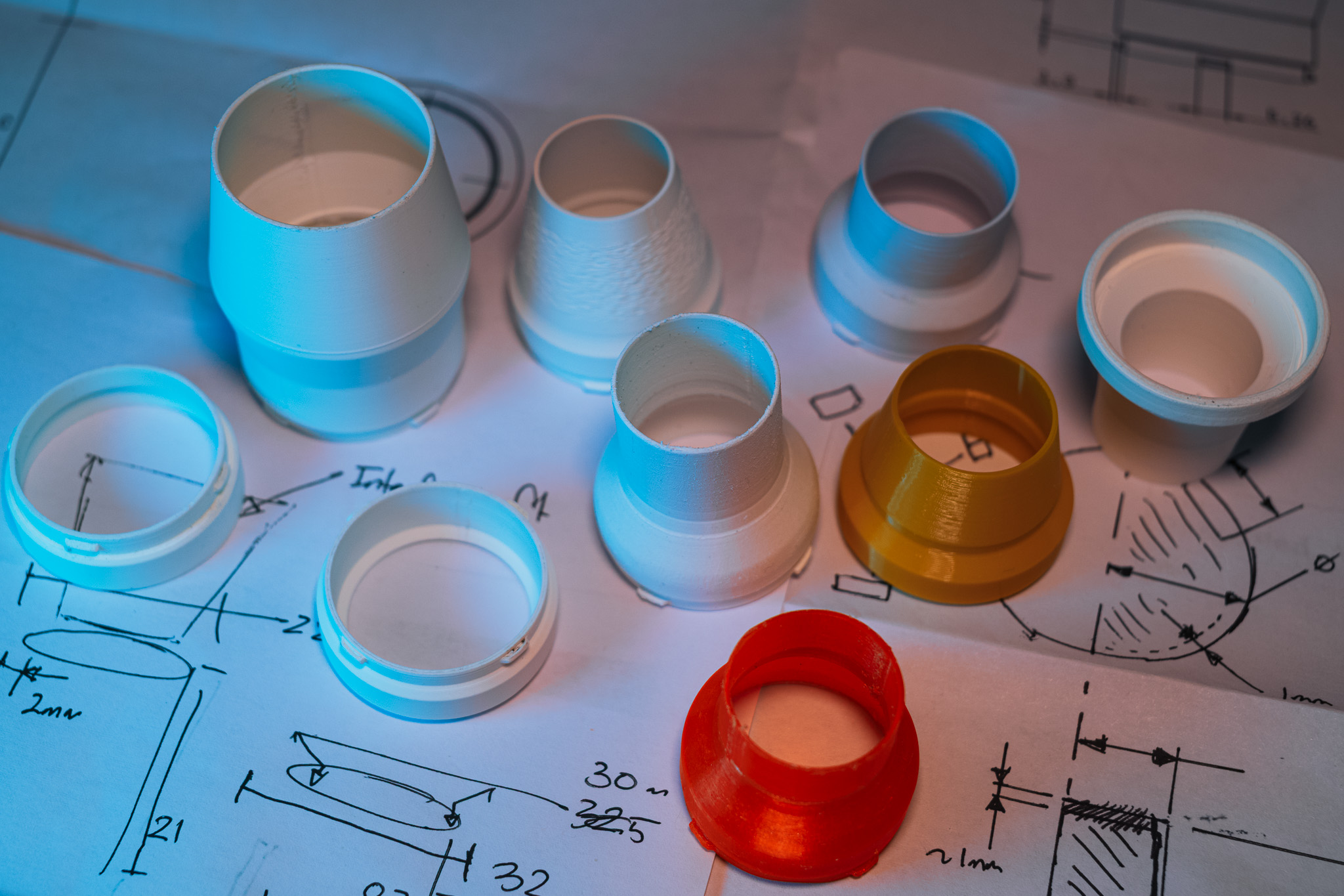 Prototype iterations on hand-drawn engineering sketches, showing the progression from early PLA and PETG versions to the final ABS-GF adapter